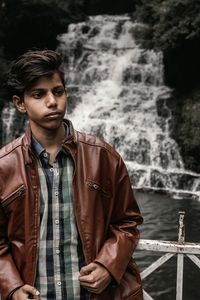 Portrait of young man standing against waterfall