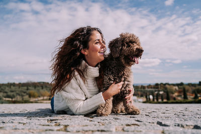 Happy young woman looking away while sitting against sky