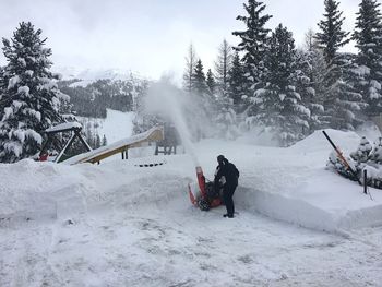 Rear view of man operating snowblower in playground