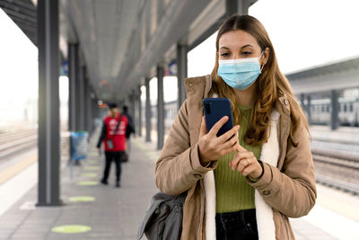 Woman wearing medical mask using smartphone on the train at station outdoors