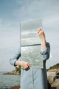 Man holding umbrella by sea against sky