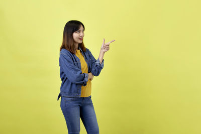 Full length of young woman standing against yellow background