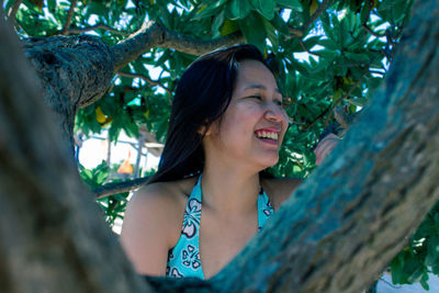Portrait of smiling young woman against tree trunk