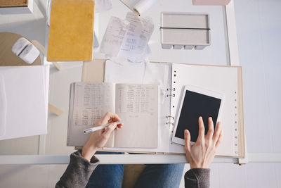 Directly above shot of female design professional with book and digital tablet at desk in workshop