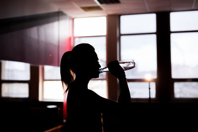 Rear view of silhouette woman drinking glass window
