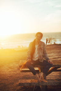 Man sitting on beach against sky during sunset