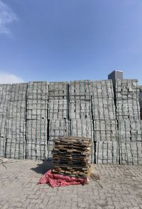 Stack of wooden wall by fence against blue sky