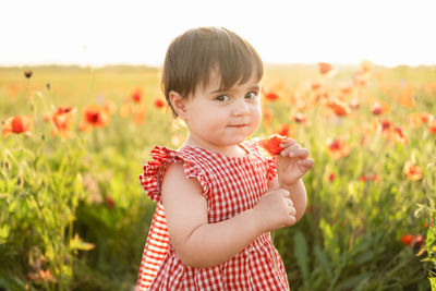 Cute baby girl with flower standing at field