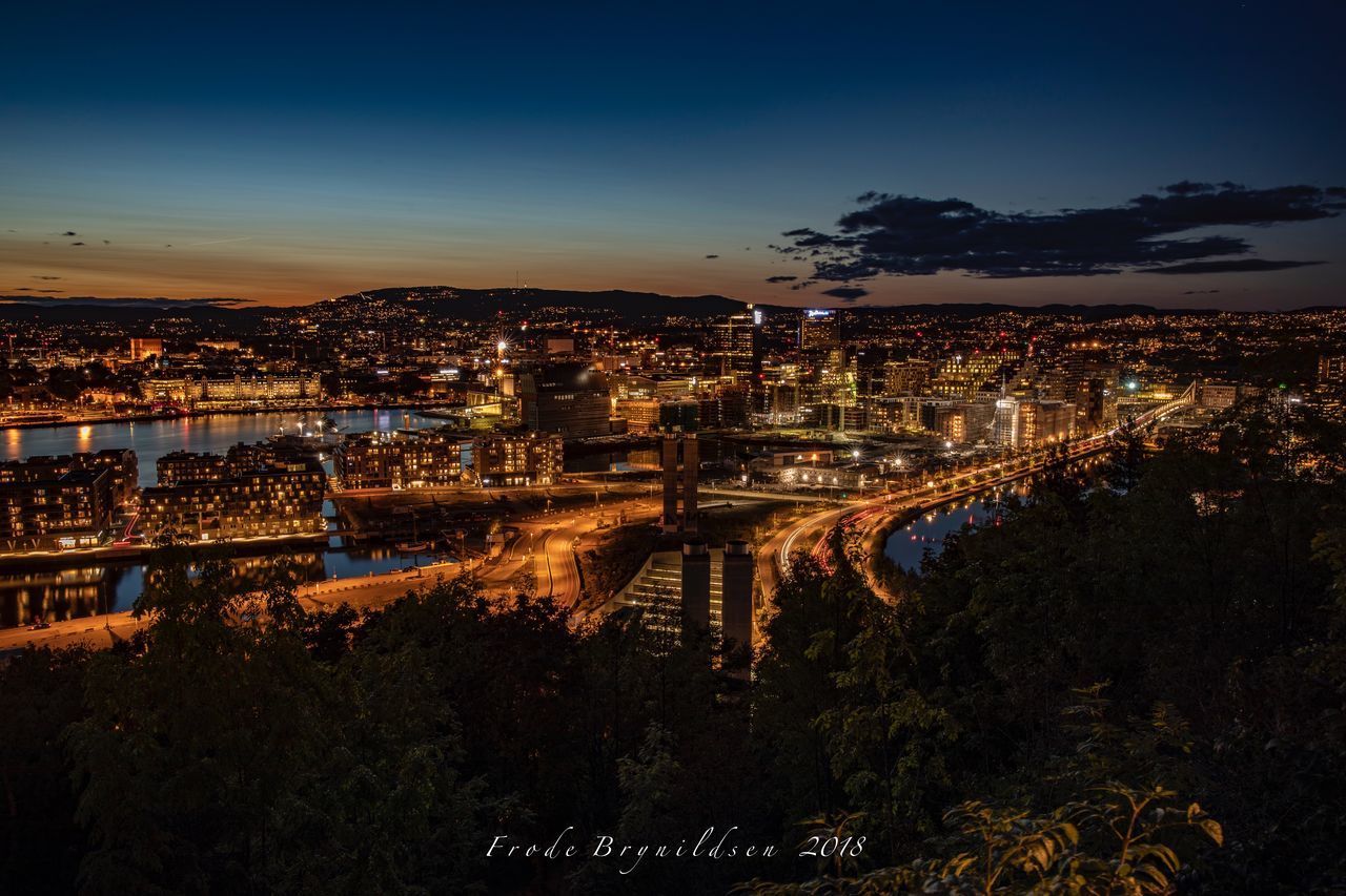 HIGH ANGLE VIEW OF ILLUMINATED BRIDGE OVER RIVER BY BUILDINGS IN CITY