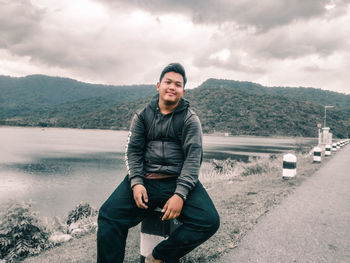 Portrait of young man sitting on mountain against sky