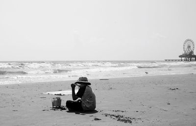 Man sitting on beach against sky