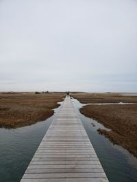 Boardwalk leading towards pier against sky