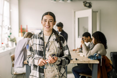 Portrait of smiling female teacher wearing plaid shirt with students in background at carpentry class