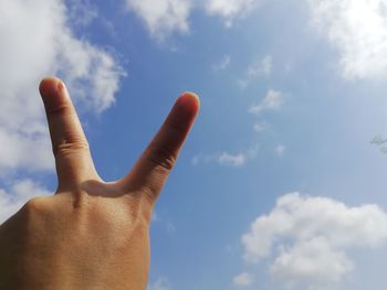 Cropped hand of woman gesturing peace sign against sky