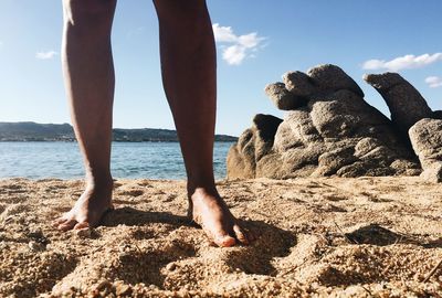 Low section of child standing on beach against sky