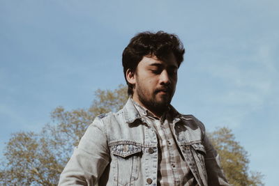 Young man looking down against sky