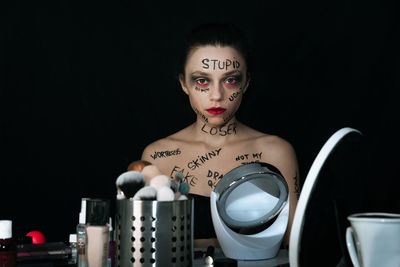 Portrait of woman with text on body sitting against black background