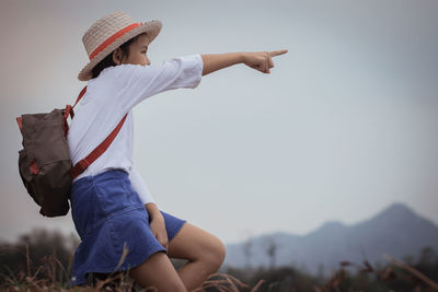 Side view of girl pointing against sky