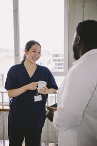 Smiling female nurse holding coffee cup while looking at doctor in hospital
