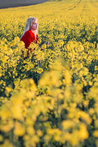 Full length of young woman with yellow flowers in field