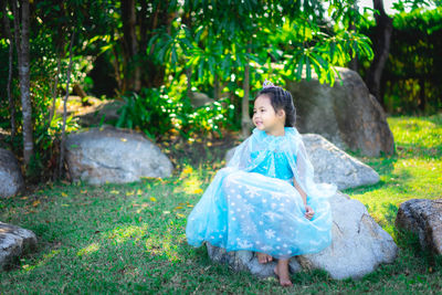 Full length of cute girl wearing dress sitting on rock in park