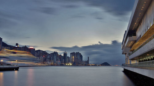 Illuminated buildings by sea against sky at dusk