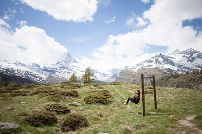 Woman swinging over landscape against sky