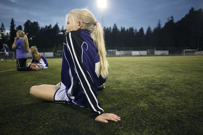 Side view of girl sitting on field against sky