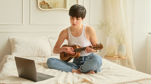 Young woman playing guitar while lying on bed at home