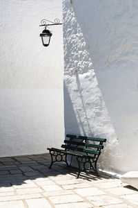 Empty bench on street by wall during sunny day