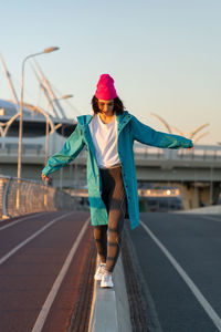 Nice cheerful girl outstretched hands to sides walking near bridge down road urban setting.