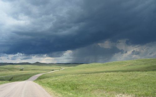 Road passing through field against cloudy sky