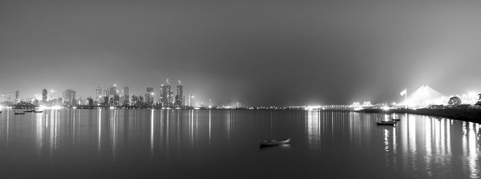 Illuminated city by sea against sky at night