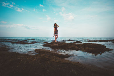 Man standing on rock at beach against sky