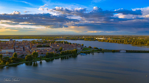 Scenic view of river by buildings against sky at sunset