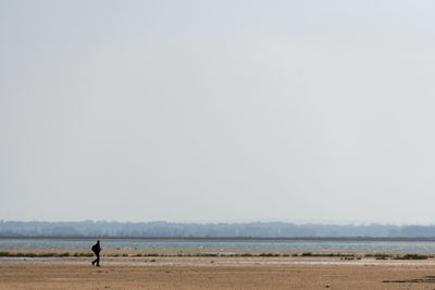 Scenic view of sea with walking man against clear sky