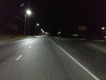 Empty road along illuminated street lights at night