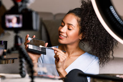 Smiling young woman holding face powder by camera at home