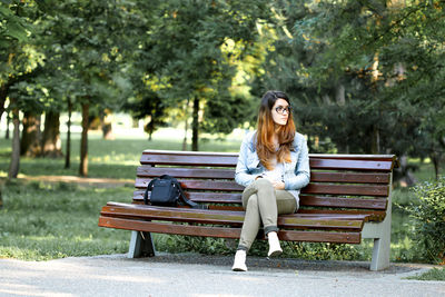 Portrait of young woman sitting on bench in park