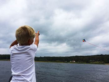 Rear view of boy standing by lake against sky