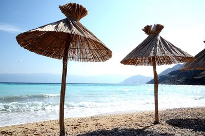 Thatched roof parasol at beach against sky