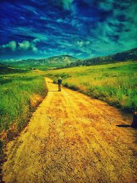 Man walking on road amidst field against sky