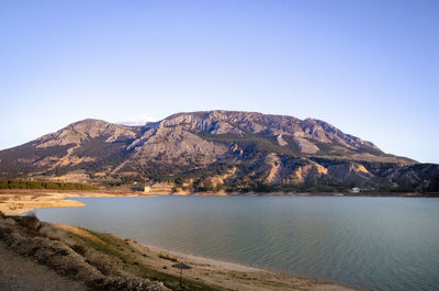 Scenic view of lake and mountains against clear blue sky