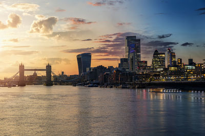 Scenic view of river by buildings against sky during sunset