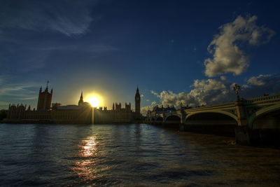 Bridge over river by buildings against sky during sunset