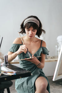 Young woman painting on canvas while sitting on table