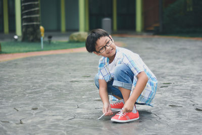 Cute boy tying shoelace while crouching on land