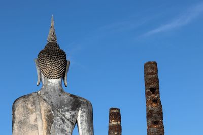 Low angle view of weathered buddha statue against blue sky