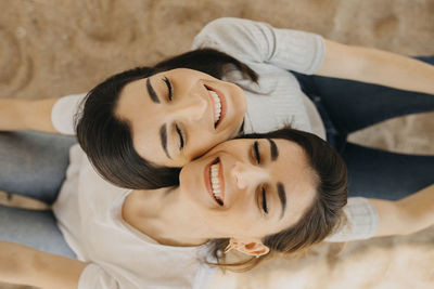 Smiling sisters with eyes closed on sand at beach