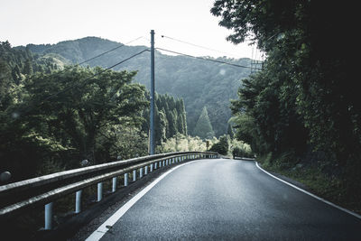 Empty road amidst trees against mountains